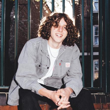 Alex sits down, smiling and looking at the camera.