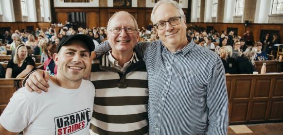 Andy, David and Craig smile in front of a room of teachers